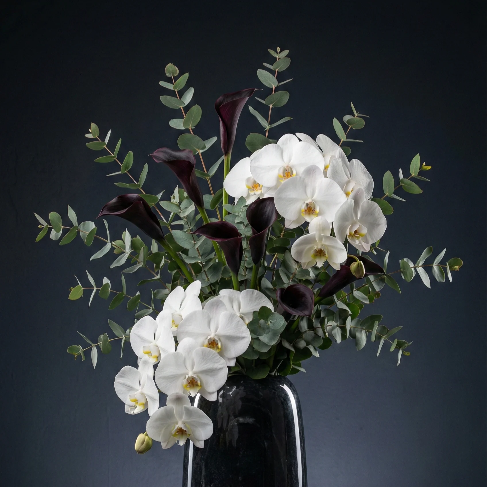 Białe orchidee i ciemne kalie w wazonie